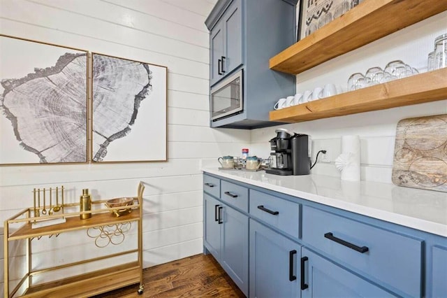kitchen with blue cabinets, light countertops, dark wood-style floors, open shelves, and stainless steel microwave