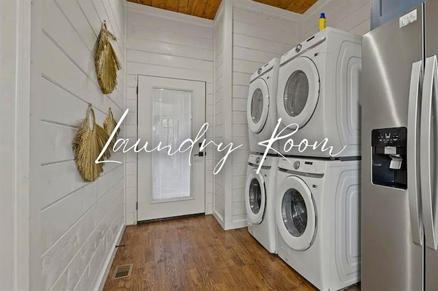 laundry area with dark wood-style flooring, visible vents, wood walls, stacked washing maching and dryer, and laundry area