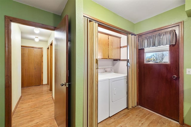 clothes washing area featuring cabinets, washing machine and dryer, and light hardwood / wood-style flooring