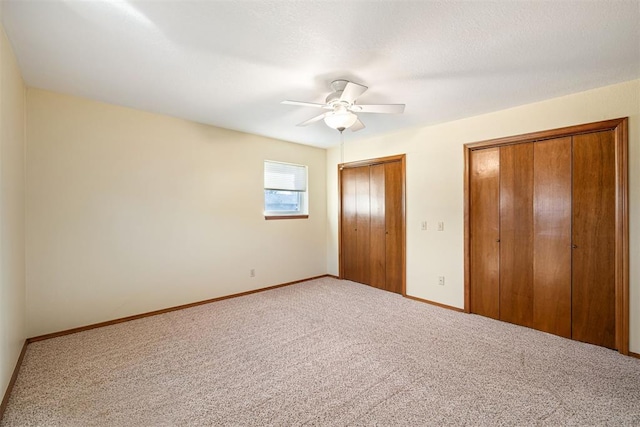 unfurnished bedroom featuring ceiling fan, carpet floors, a textured ceiling, and two closets