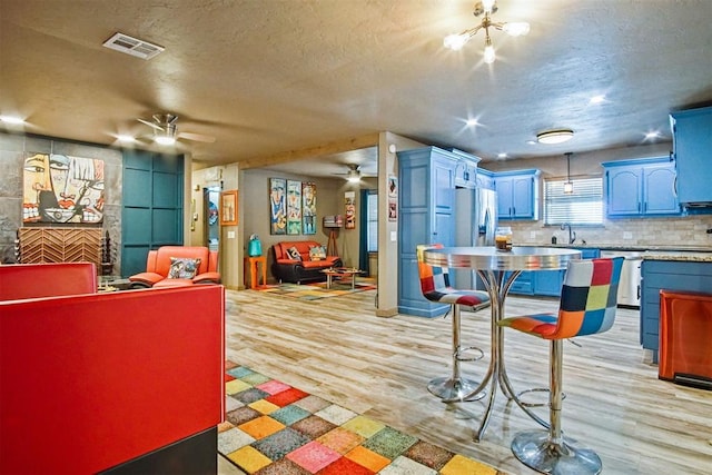 kitchen featuring visible vents, a ceiling fan, a sink, light wood-type flooring, and backsplash