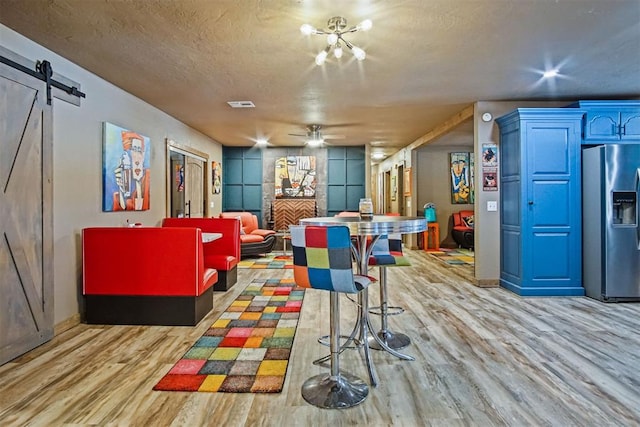 playroom featuring a barn door, visible vents, ceiling fan, a textured ceiling, and light wood-style floors