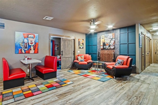 recreation room featuring a ceiling fan, a textured ceiling, visible vents, and wood finished floors