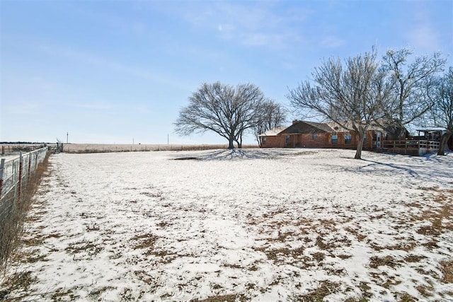 snowy yard with a rural view and fence