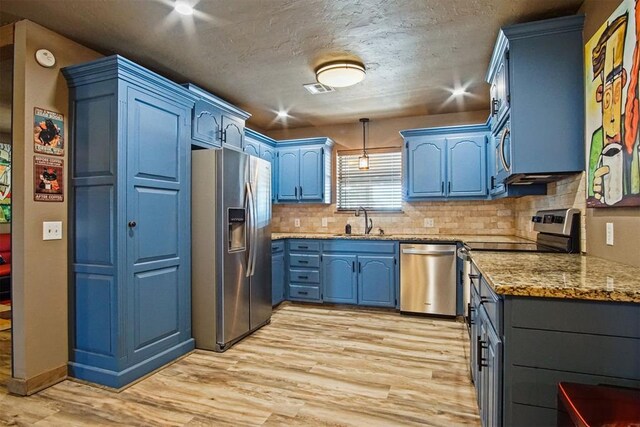 kitchen featuring light wood-style flooring, blue cabinets, hanging light fixtures, stainless steel appliances, and a sink