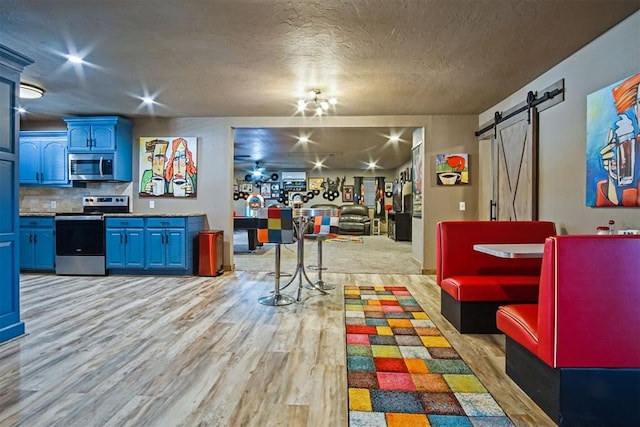 interior space with blue cabinets, light wood-style flooring, tasteful backsplash, stainless steel appliances, and a barn door