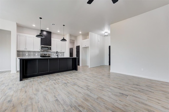 kitchen featuring an island with sink, stainless steel appliances, decorative light fixtures, backsplash, and white cabinets