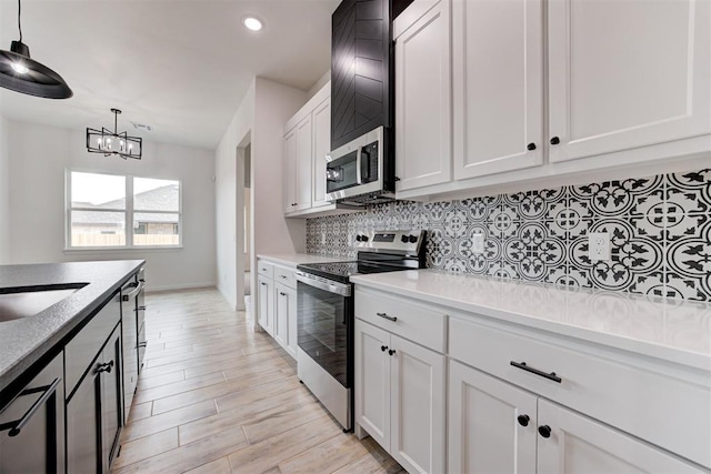 kitchen featuring stainless steel appliances, hanging light fixtures, light hardwood / wood-style floors, tasteful backsplash, and white cabinets