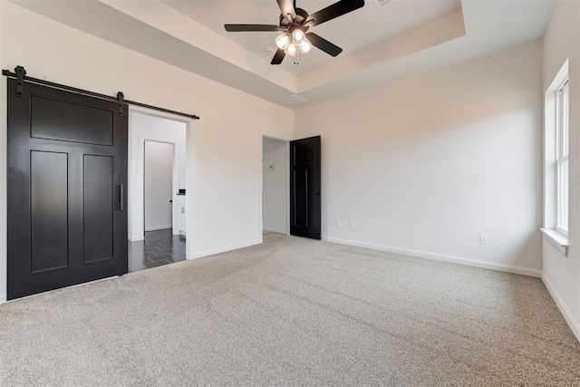 unfurnished bedroom featuring dark carpet, ceiling fan, a tray ceiling, and a barn door