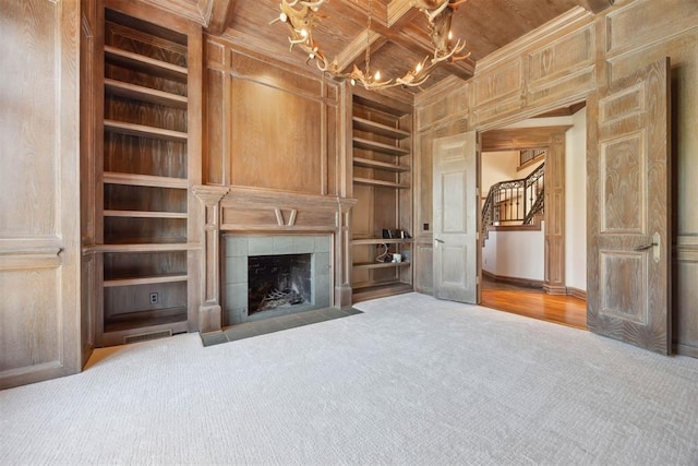 unfurnished living room with a tile fireplace, built in shelves, coffered ceiling, ornamental molding, and carpet