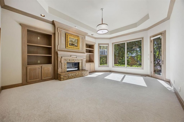 unfurnished living room with a stone fireplace, crown molding, a tray ceiling, light colored carpet, and built in features