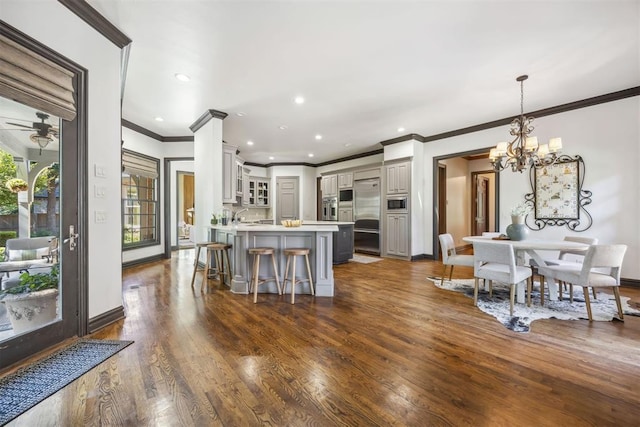 kitchen with built in appliances, gray cabinetry, a breakfast bar area, pendant lighting, and dark hardwood / wood-style flooring