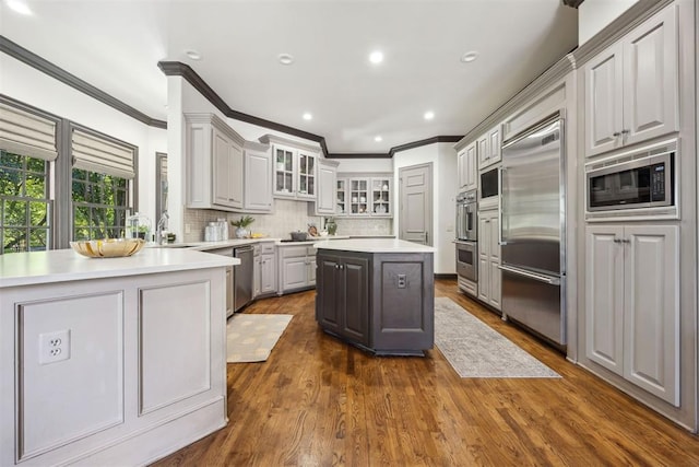 kitchen with a center island, built in appliances, sink, dark wood-type flooring, and decorative backsplash