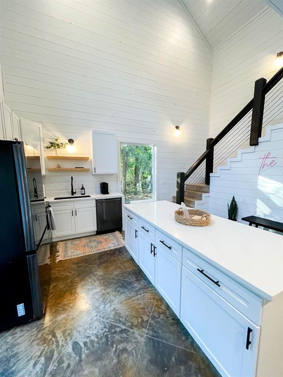 kitchen featuring light countertops, white cabinetry, vaulted ceiling, a sink, and black appliances