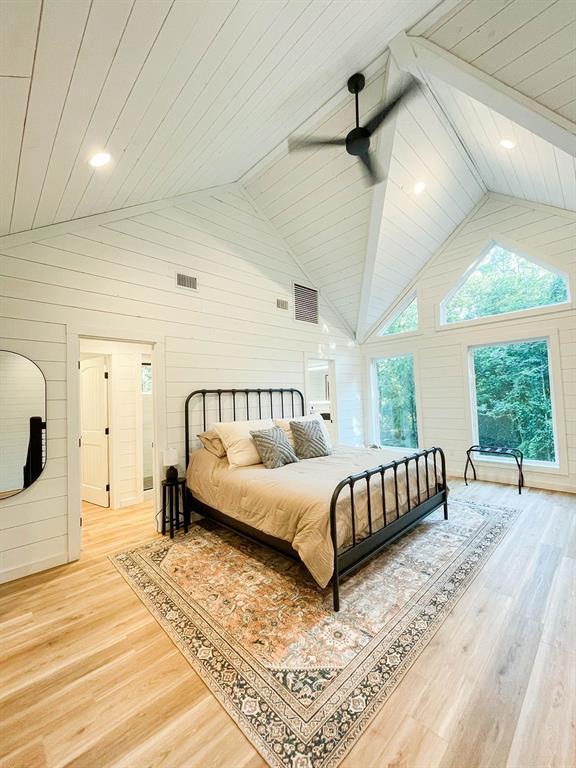 bedroom featuring light wood finished floors, visible vents, wooden walls, and high vaulted ceiling