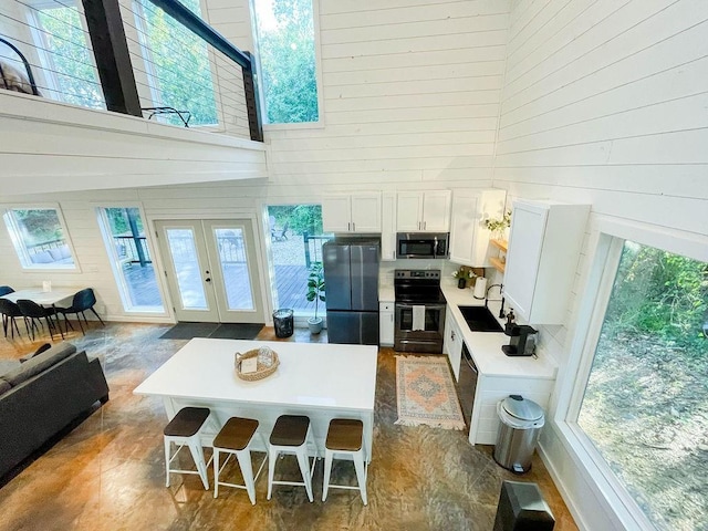 kitchen with appliances with stainless steel finishes, wood walls, a high ceiling, and white cabinetry
