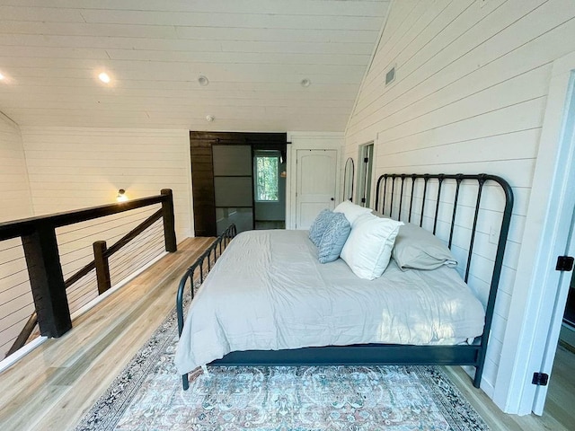 bedroom featuring high vaulted ceiling, wooden walls, and wood finished floors