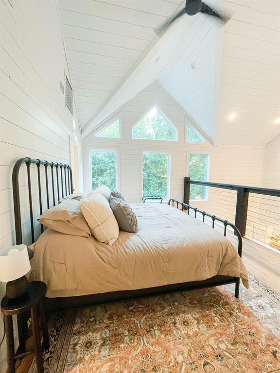 bedroom featuring multiple windows, high vaulted ceiling, wood finished floors, and beamed ceiling