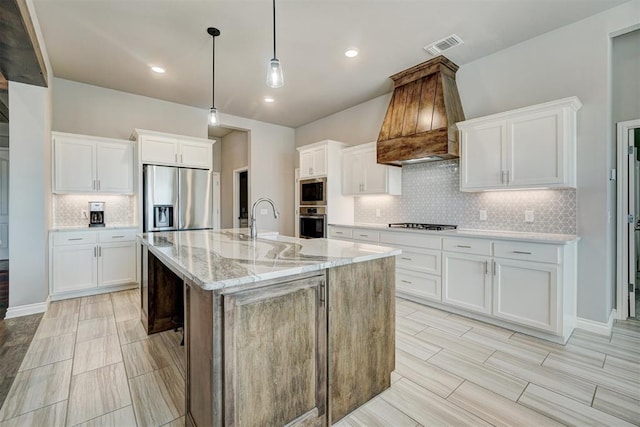 kitchen with white cabinets, appliances with stainless steel finishes, a center island with sink, and light stone countertops