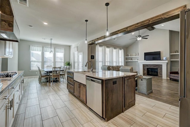 kitchen featuring a center island with sink, hanging light fixtures, stainless steel appliances, a fireplace, and sink