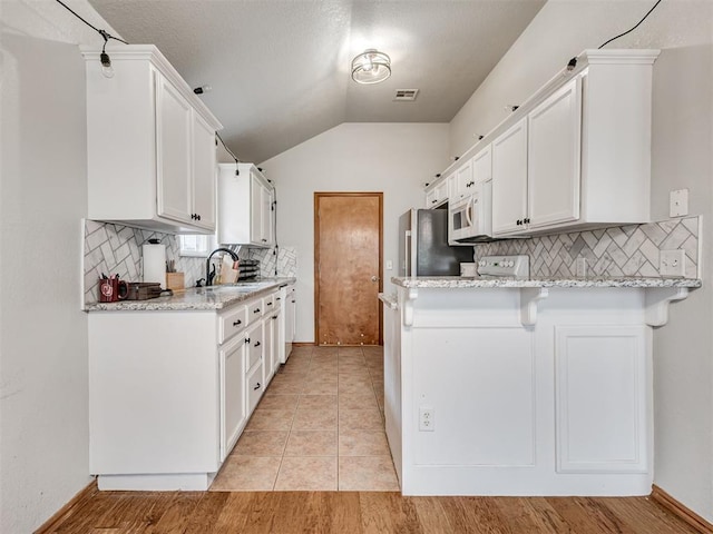 kitchen featuring visible vents, white cabinets, light stone counters, a peninsula, and a sink