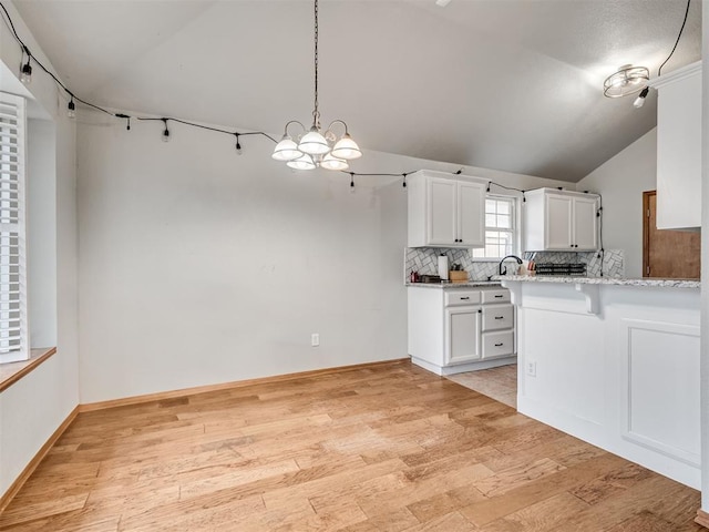 kitchen featuring light wood-type flooring, white cabinets, vaulted ceiling, and backsplash