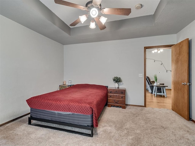 bedroom with carpet floors, a tray ceiling, baseboards, and a ceiling fan