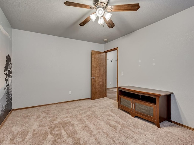 unfurnished bedroom featuring carpet floors, a textured ceiling, baseboards, and a ceiling fan