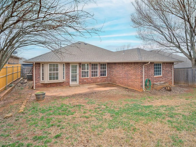 back of property featuring a shingled roof, a patio, a fenced backyard, a yard, and brick siding