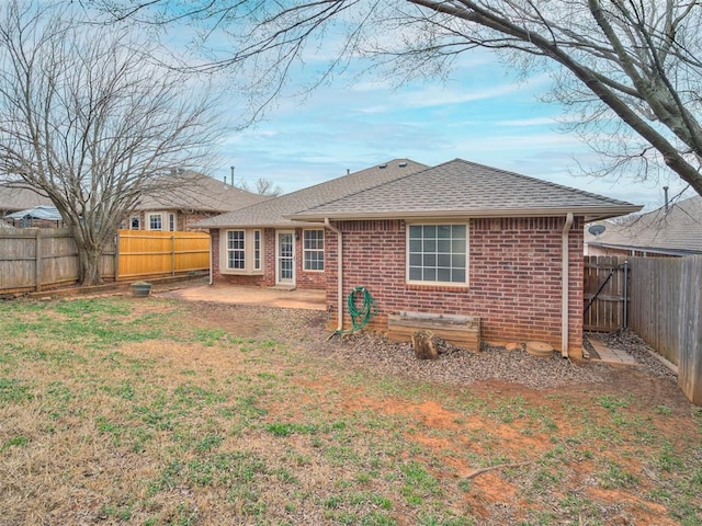 back of property featuring brick siding, a yard, a patio, a shingled roof, and a fenced backyard