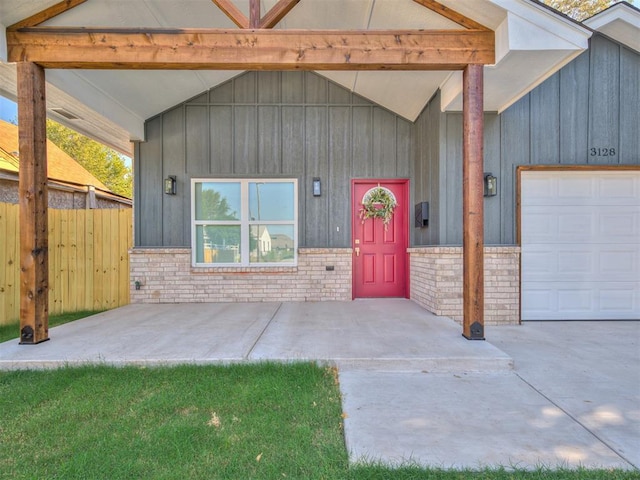 view of exterior entry with a garage, fence, board and batten siding, and brick siding