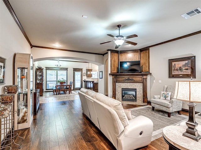 living room featuring ceiling fan, a large fireplace, dark hardwood / wood-style floors, and ornamental molding