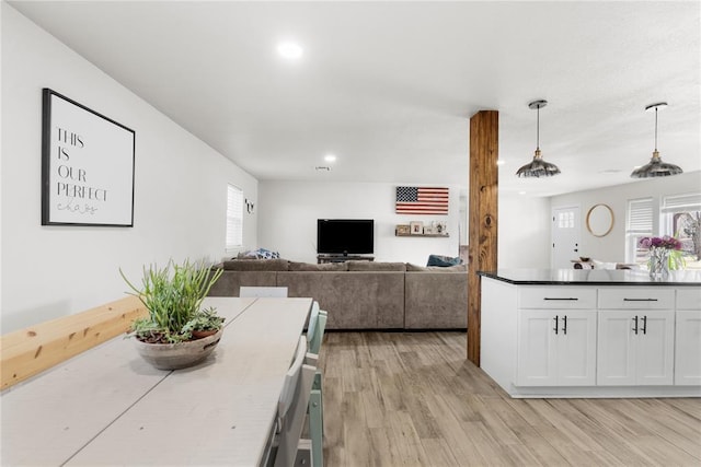 kitchen featuring light wood finished floors, dark countertops, open floor plan, hanging light fixtures, and white cabinetry