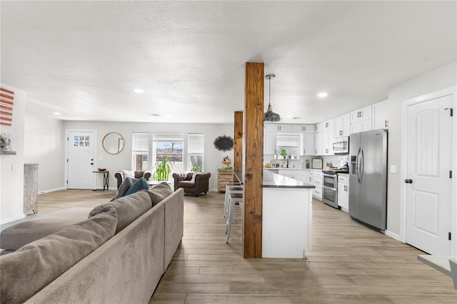 kitchen with appliances with stainless steel finishes, open floor plan, white cabinets, light wood-type flooring, and a peninsula