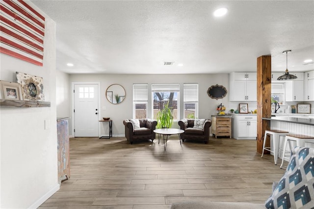 living area with a textured ceiling, light wood-type flooring, visible vents, and baseboards