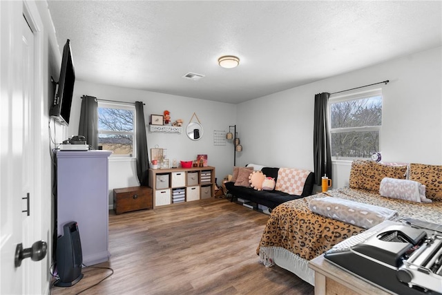 bedroom with a textured ceiling, multiple windows, wood finished floors, and visible vents