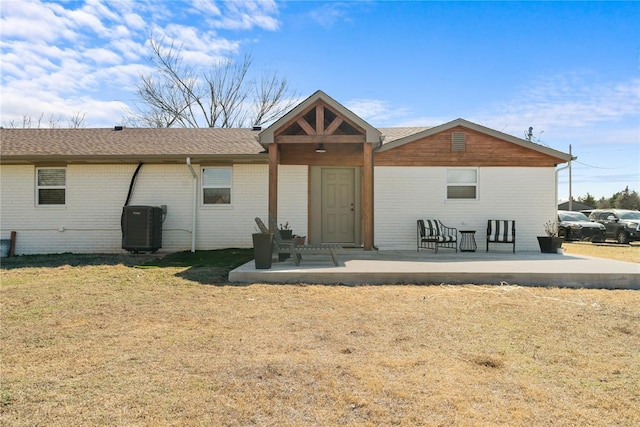 back of property featuring a yard, brick siding, central AC, and a patio