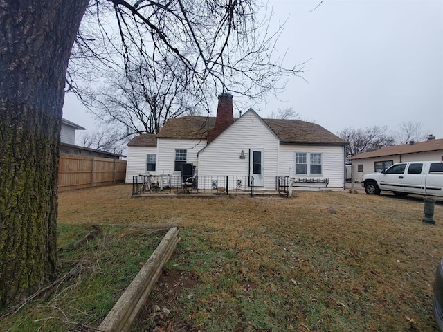 back of property with a chimney, fence, and a yard