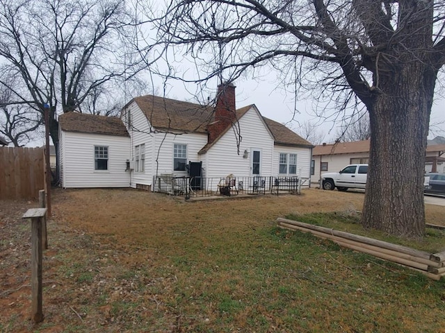 rear view of house featuring a yard, a chimney, and fence