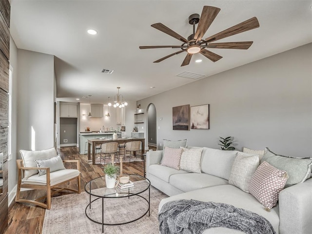 living area featuring dark wood-style floors, arched walkways, recessed lighting, visible vents, and ceiling fan with notable chandelier