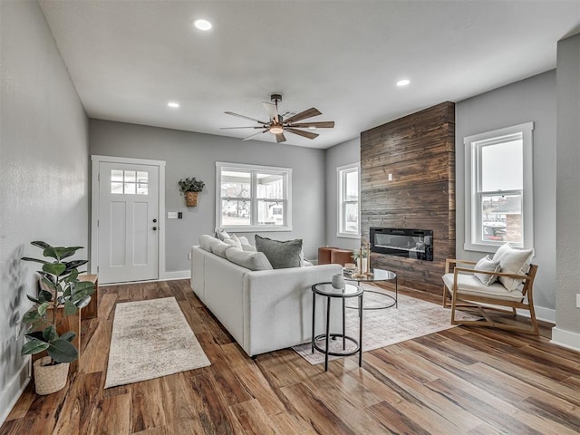 living area featuring a large fireplace, baseboards, wood finished floors, and recessed lighting