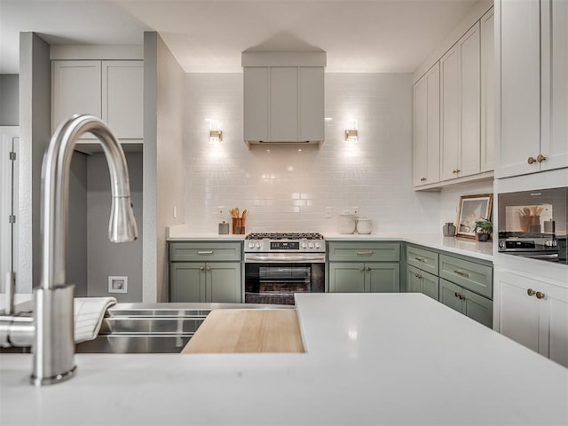 kitchen with light countertops, stainless steel gas range, backsplash, and green cabinetry