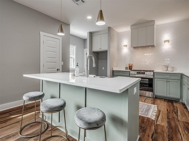 kitchen with stainless steel range with gas cooktop, light countertops, and an island with sink