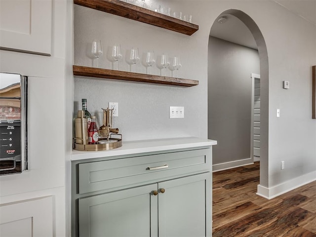 bar with arched walkways, a bar, dark wood-style flooring, and baseboards