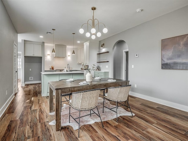 dining room featuring arched walkways, wood finished floors, visible vents, and baseboards