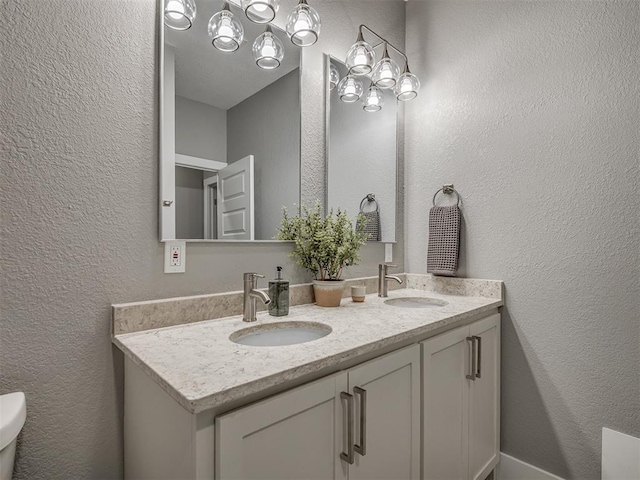 bathroom featuring a textured wall, a sink, toilet, and double vanity