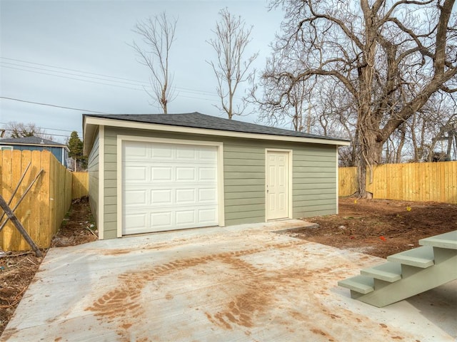 detached garage featuring concrete driveway and fence