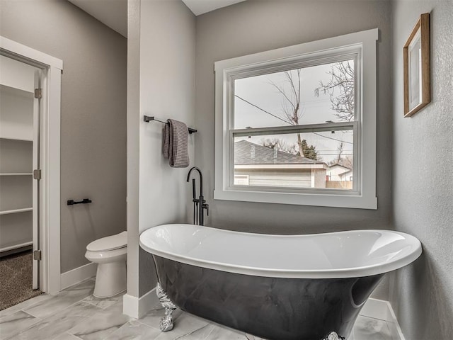 1413 NE 14th St, Oklahoma City, OK 73117 - bathroom with toilet, a soaking tub, baseboards, and marble look tile flooring