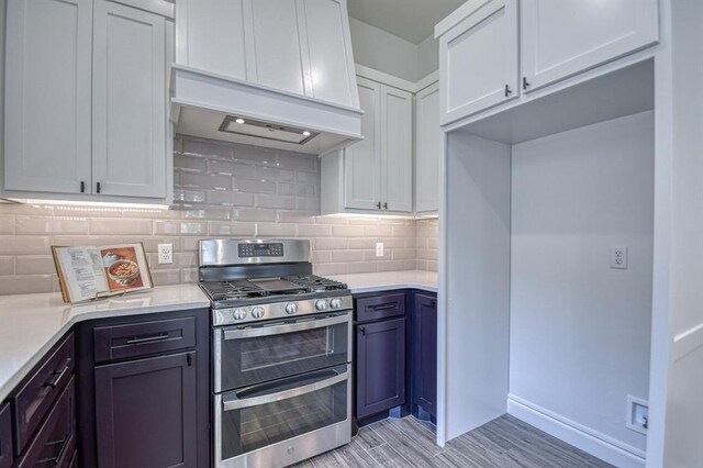 kitchen with custom range hood, double oven range, backsplash, white cabinets, and light countertops