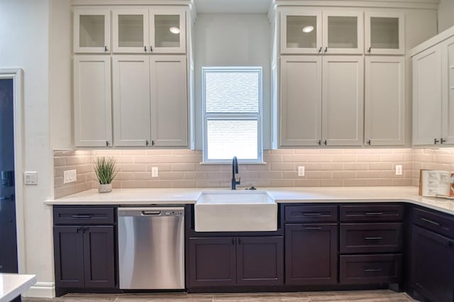 kitchen with backsplash, light countertops, stainless steel dishwasher, white cabinets, and a sink